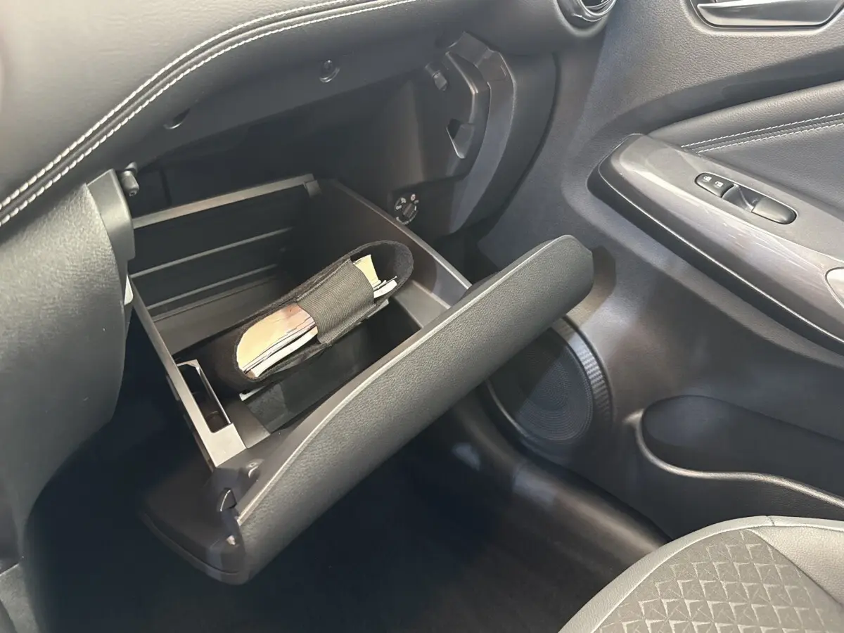 Vue intérieure côté passager du Nissan Juke 2023, boîte à gants ouverte avec rangement visible, sellerie noire.