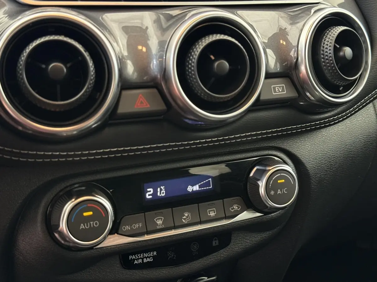 Détail du tableau de bord noir du Nissan Juke 2023 montrant les aérateurs ronds et la commande de climatisation digitale à 21,6°C.