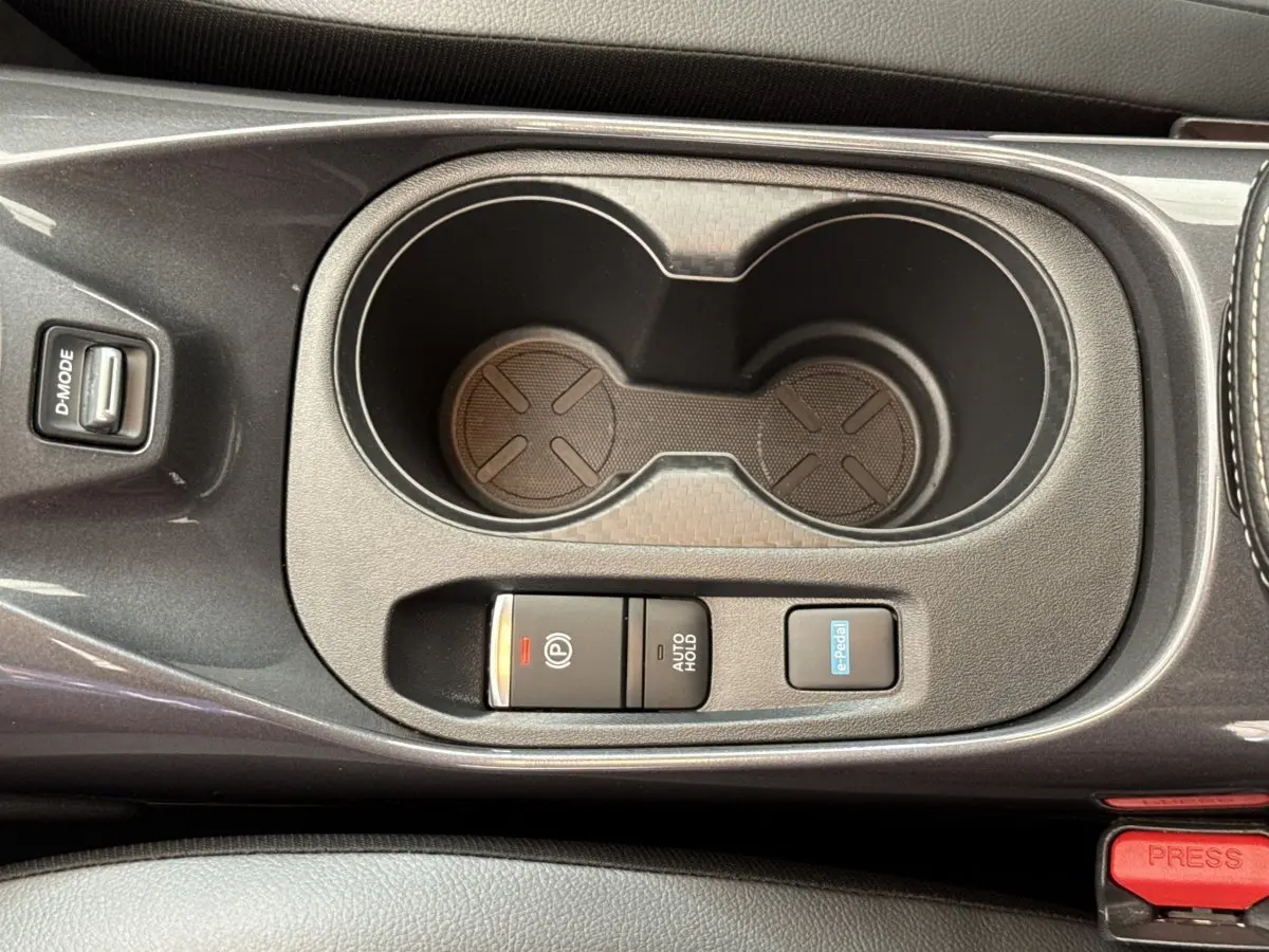 Vue rapprochée de la console centrale grise foncée du Nissan Juke 2023, avec porte-gobelets et boutons de frein électrique et e-Pedal.