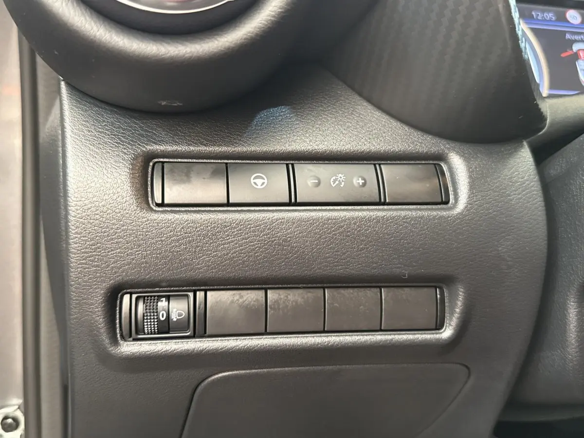 Détail des commandes de réglage des phares et tableau de bord côté conducteur dans un Nissan Juke gris foncé 2023.
