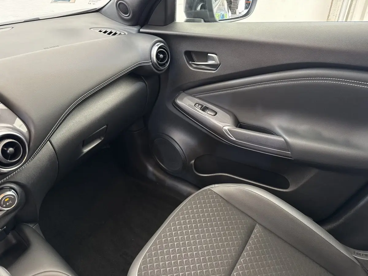 Vue intérieure côté passager du Nissan Juke 2023 gris foncé, avec tableau de bord et porte en cuir noir.