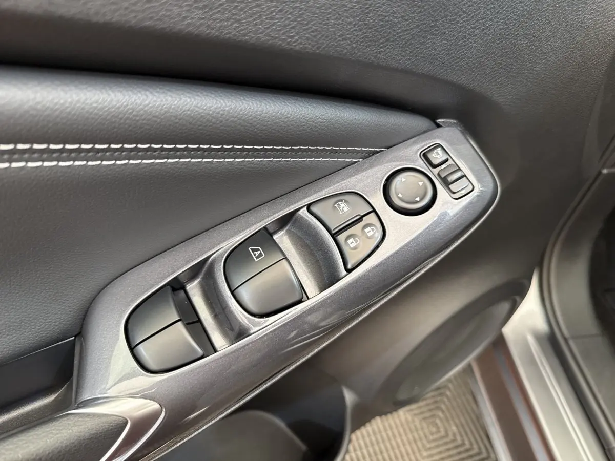 Gros plan sur la commande des vitres et rétroviseurs côté conducteur du Nissan Juke gris foncé 2023.