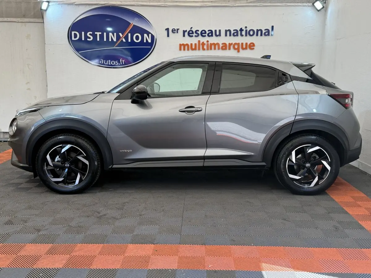 Vue de profil côté gauche d'un Nissan Juke gris foncé hybride 2023 avec jantes noires et toit noir contrasté.