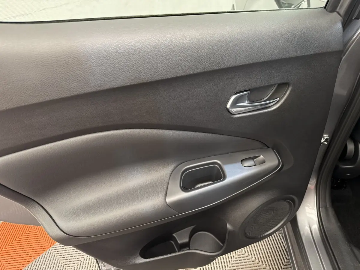 Vue rapprochée de la porte avant droite gris foncé du Nissan Juke 2023, avec poignée intérieure et commande de vitre.