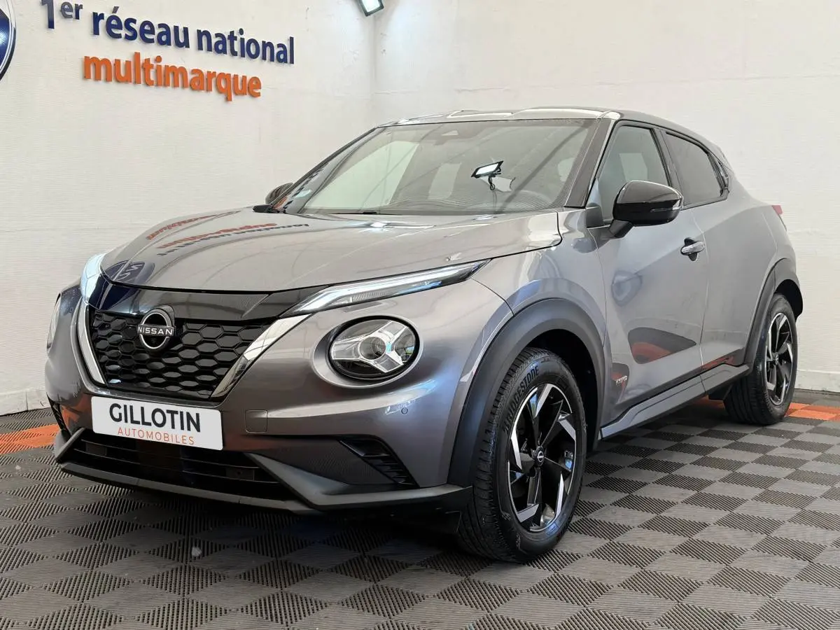 Nissan Juke gris foncé vue 3/4 avant droit, avec calandre noire et jantes alliage bicolores.