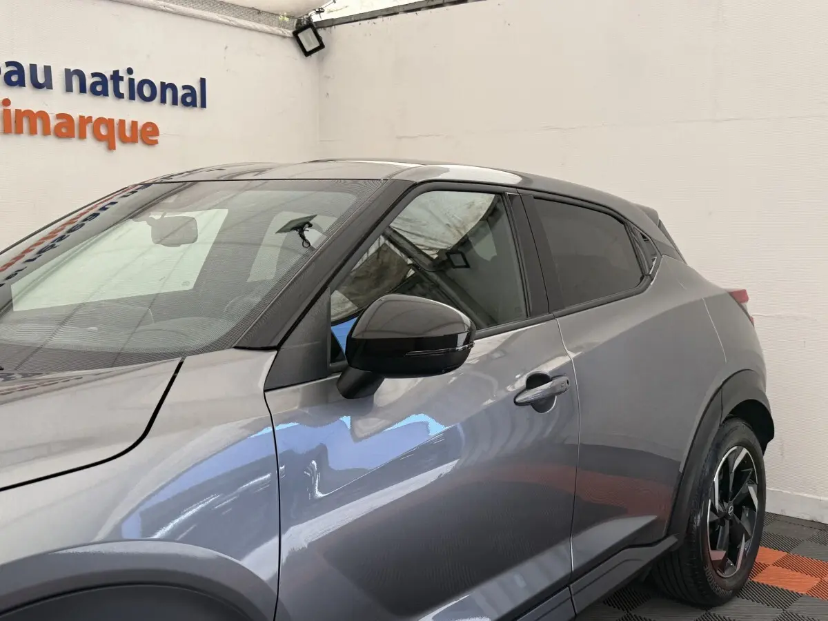 Vue de profil côté gauche du Nissan Juke 2023 gris foncé avec rétroviseur noir et jante alliage distinctive.