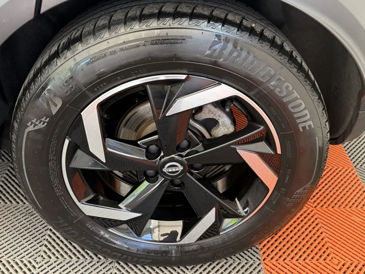 Gros plan sur la roue avant droite d’un Nissan Juke gris foncé, jante alliage noire et argentée au design anguleux.