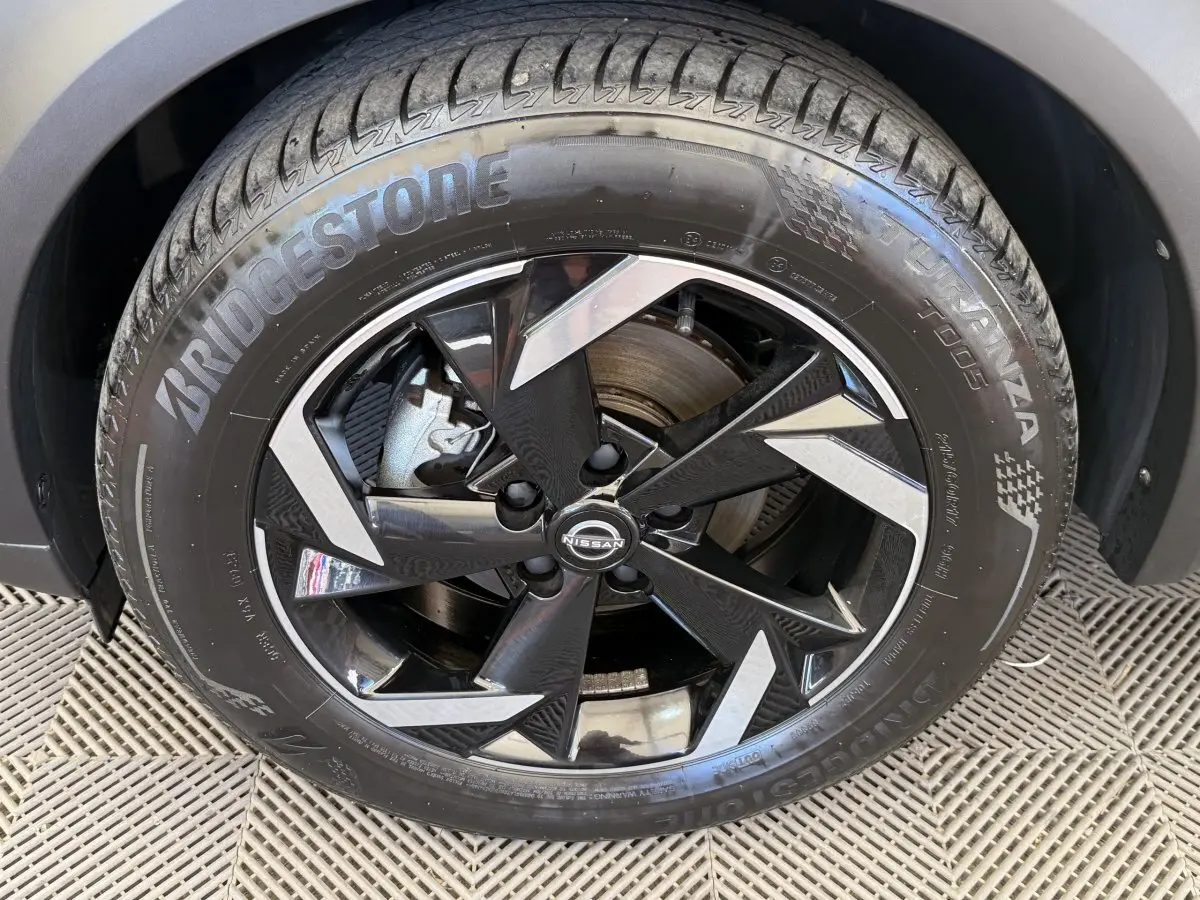 Gros plan sur la roue avant droite d’un Nissan Juke gris foncé, jante alliage noire et argentée, pneu Bridgestone.