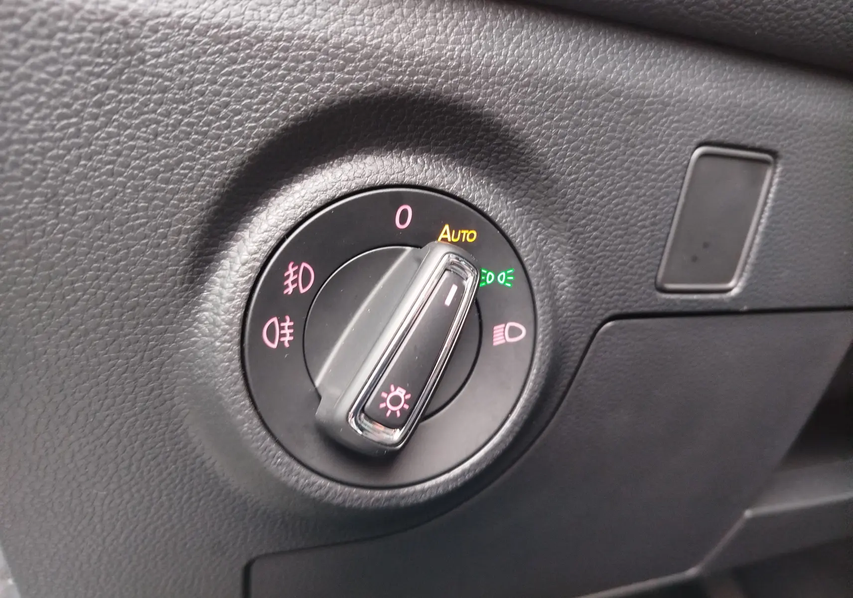 Gros plan sur le sélecteur de phares du tableau de bord en plastique noir texturé d'une SEAT ARONA 2020.