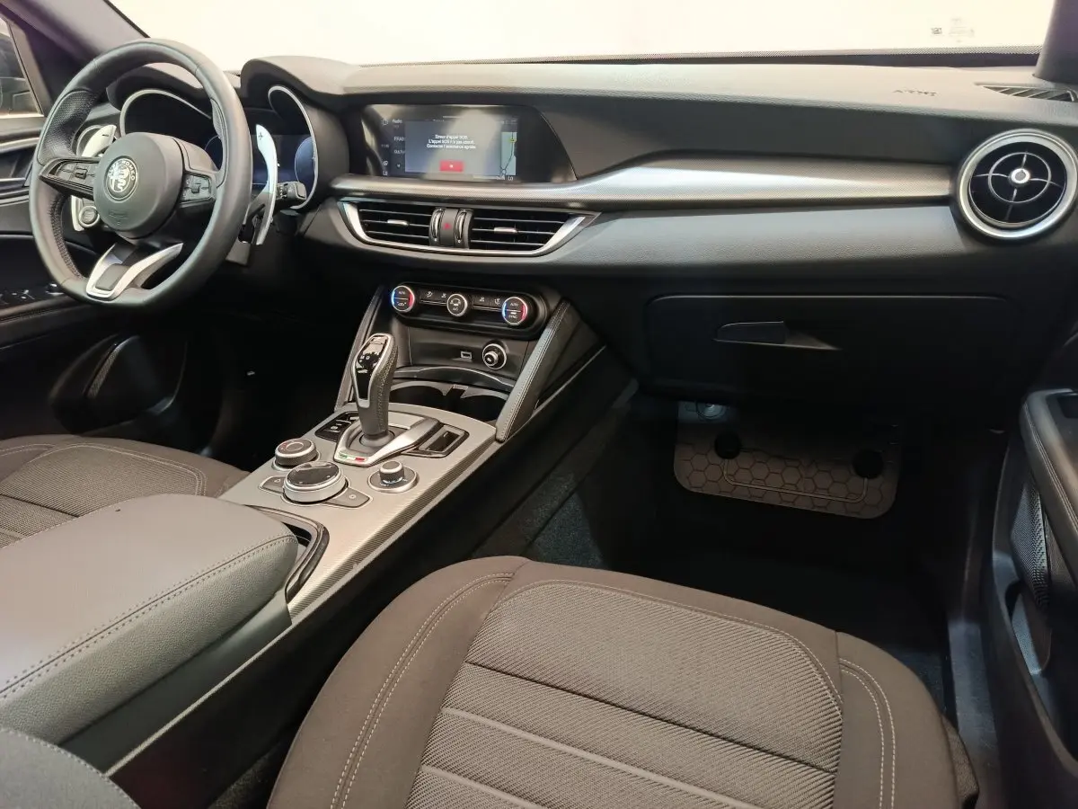 Intérieur de l'Alfa Romeo Stelvio 2024 vu côté passager, avec tableau de bord noir et console centrale moderne.