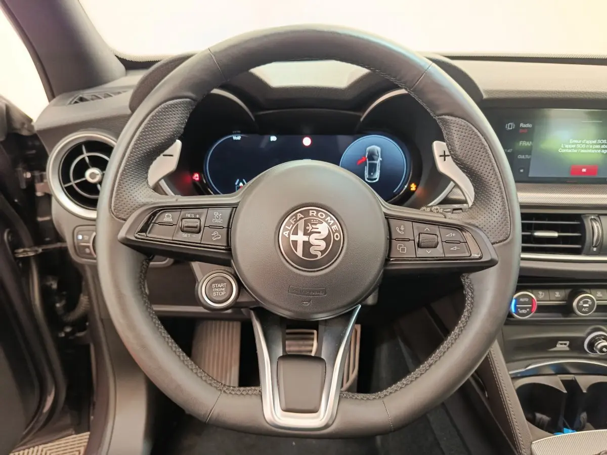 Vue rapprochée du volant cuir noir de l'Alfa Romeo Stelvio 2024 avec tableau de bord digital et commandes intégrées.