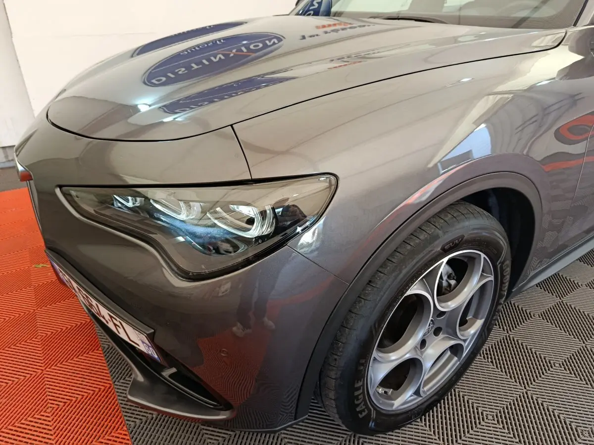 Gros plan sur l'avant droit gris foncé de l'Alfa Romeo Stelvio 2024, mettant en valeur son phare LED et sa jante distinctive.