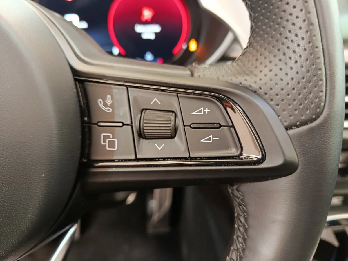 Gros plan sur les commandes du volant en cuir perforé de l'Alfa Romeo Stelvio Sprint 2024, tableau de bord flou en arrière-plan.