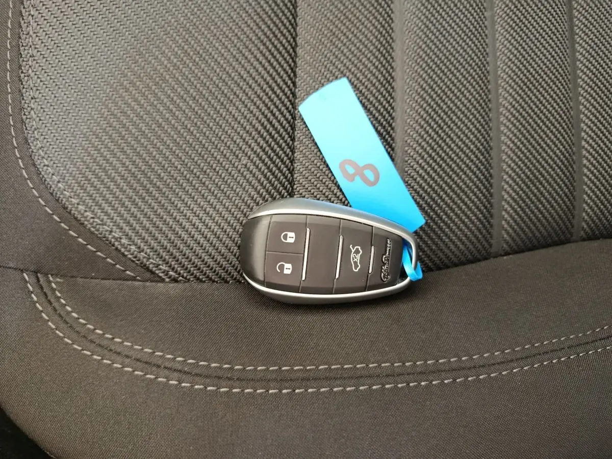 Gros plan sur la clé noire avec étiquette bleue posée sur un siège tissu gris foncé de l'Alfa Romeo Stelvio.