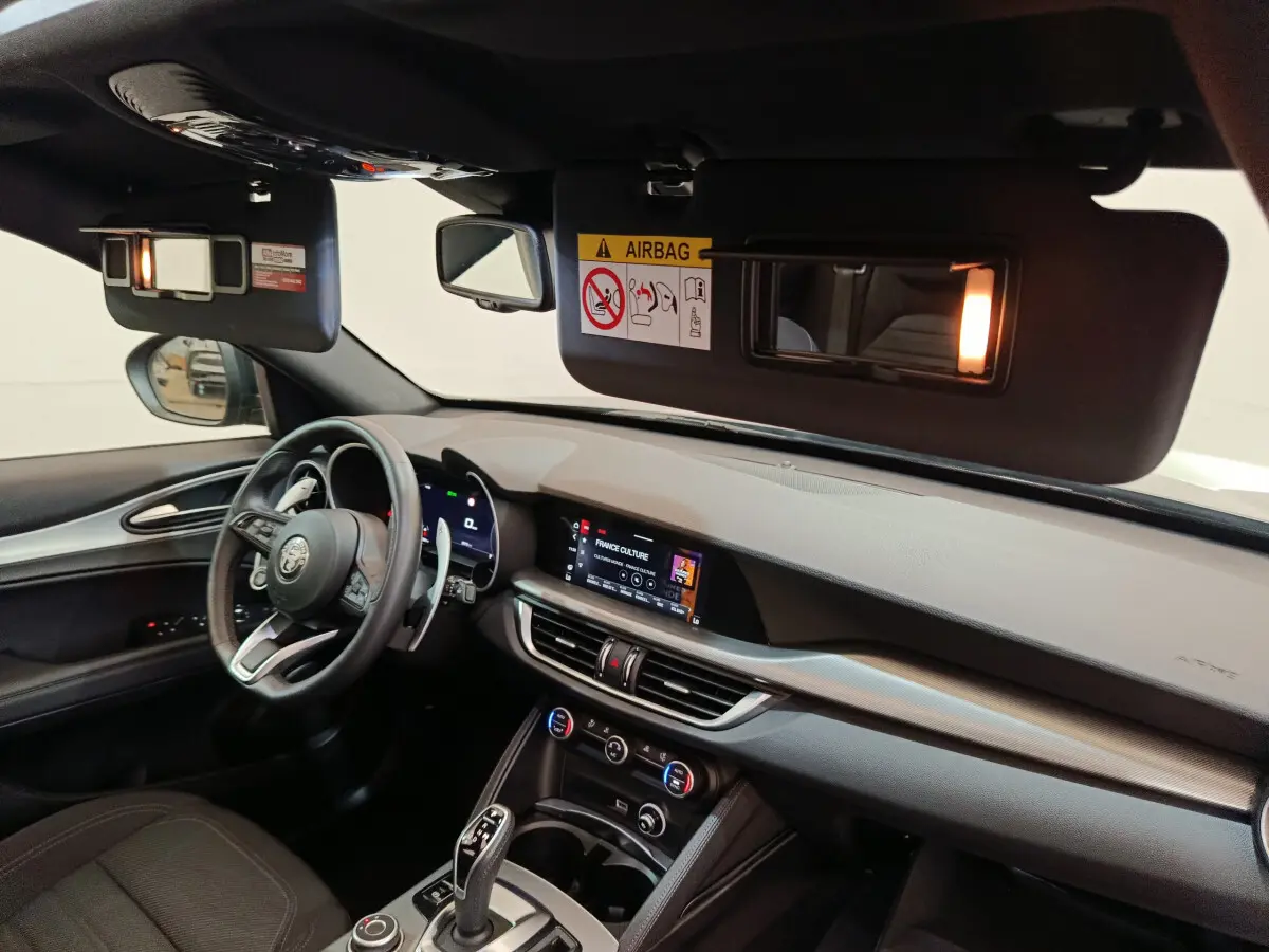 Intérieur de l'Alfa Romeo Stelvio 2024 vu côté conducteur, tableau de bord moderne avec écran tactile allumé.