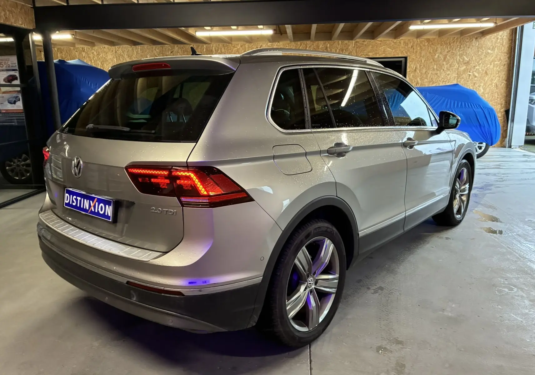 Vue 3/4 arrière droite d'un Volkswagen Tiguan gris 2.0 TDI 150 Carat avec feux arrière allumés en intérieur.