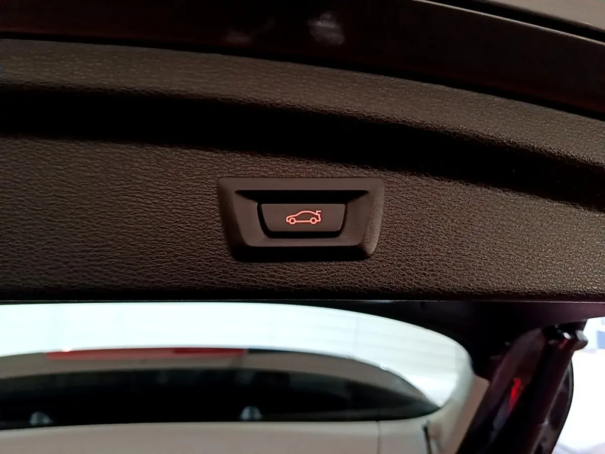 Gros plan sur le bouton d'ouverture électrique du coffre du BMW X2 sDrive18i Lounge DKG7 gris foncé, vue intérieure arrière.