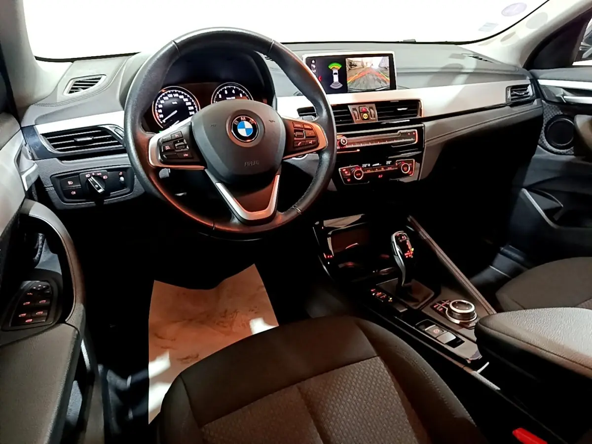 Vue intérieure côté conducteur du tableau de bord et console centrale de la BMW X2 sDrive18i Lounge DKG7, avec écran multimédia allumé.