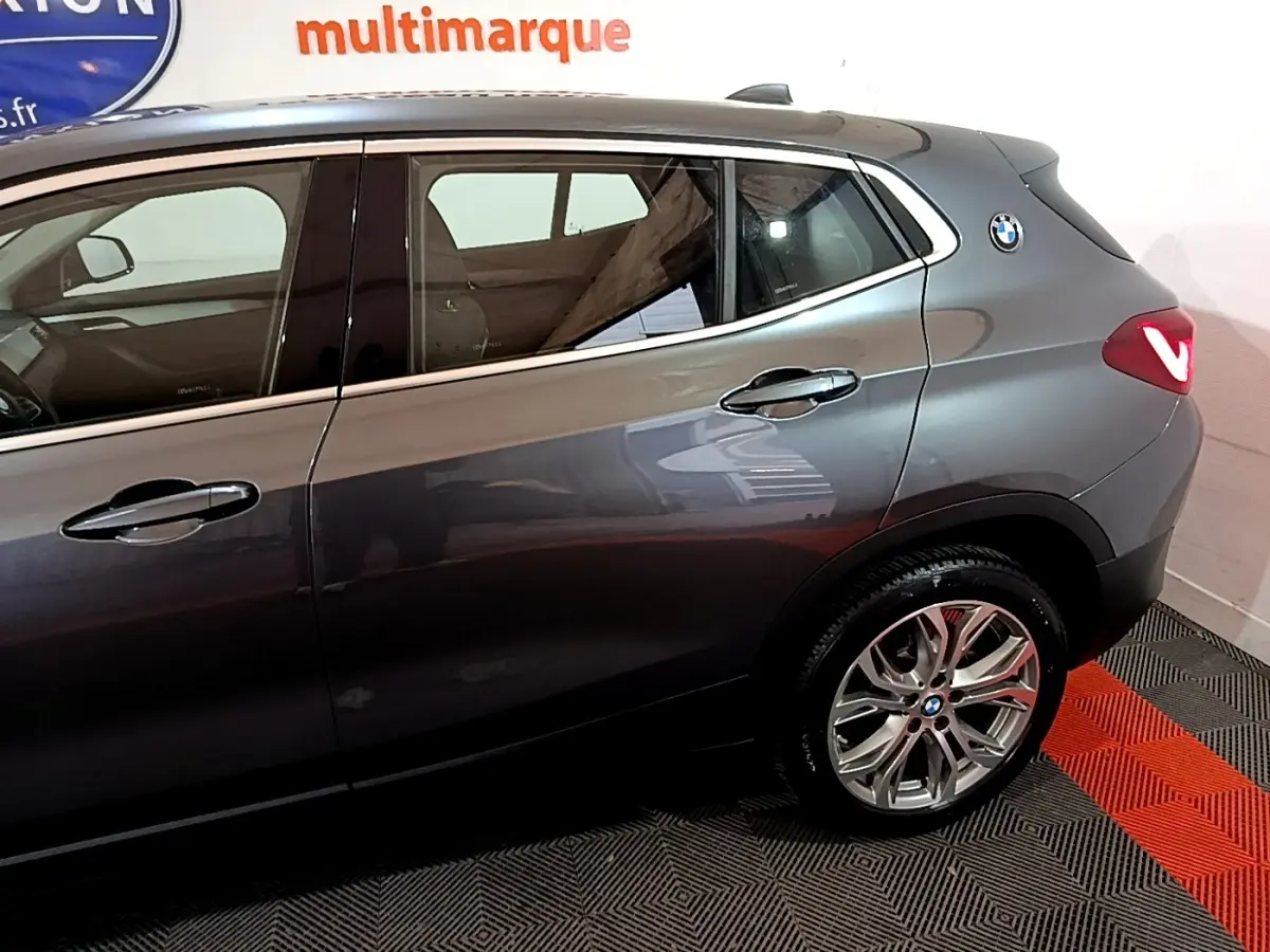 Vue latérale droite d'un BMW X2 gris foncé avec jantes alliage et logo rond sur l'aile arrière.