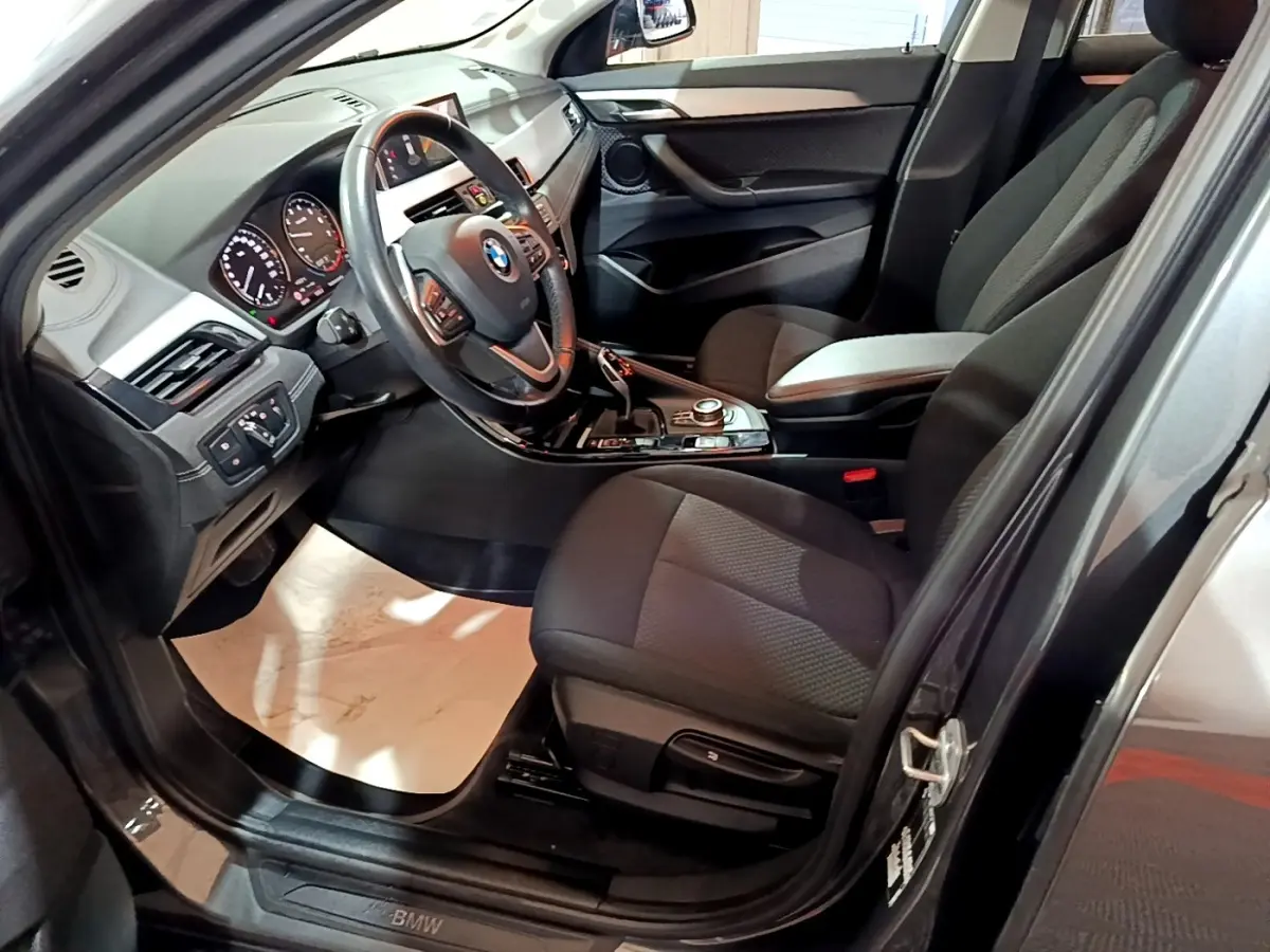 Vue intérieure côté conducteur du BMW X2 gris foncé, montrant le volant cuir multifonctions et la console centrale.