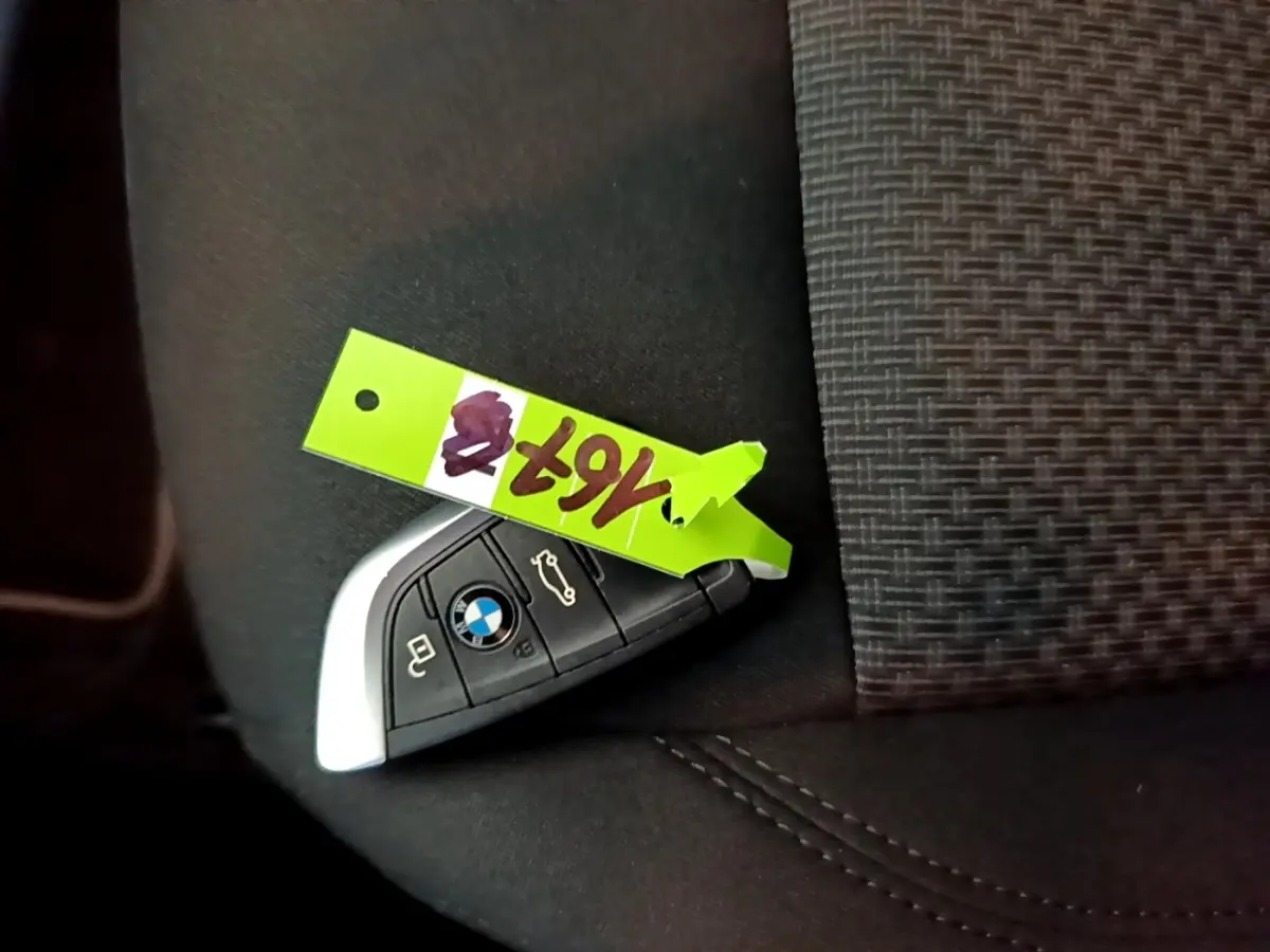 Clé de voiture BMW posée sur un siège en tissu gris foncé, avec un porte-étiquette vert fluo.