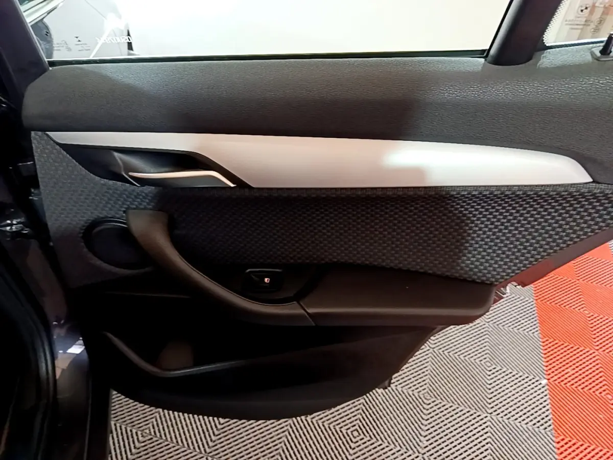 Vue intérieure du panneau de porte arrière gauche du BMW X2 sDrive18i Lounge gris foncé avec habillage texturé et insert argenté.