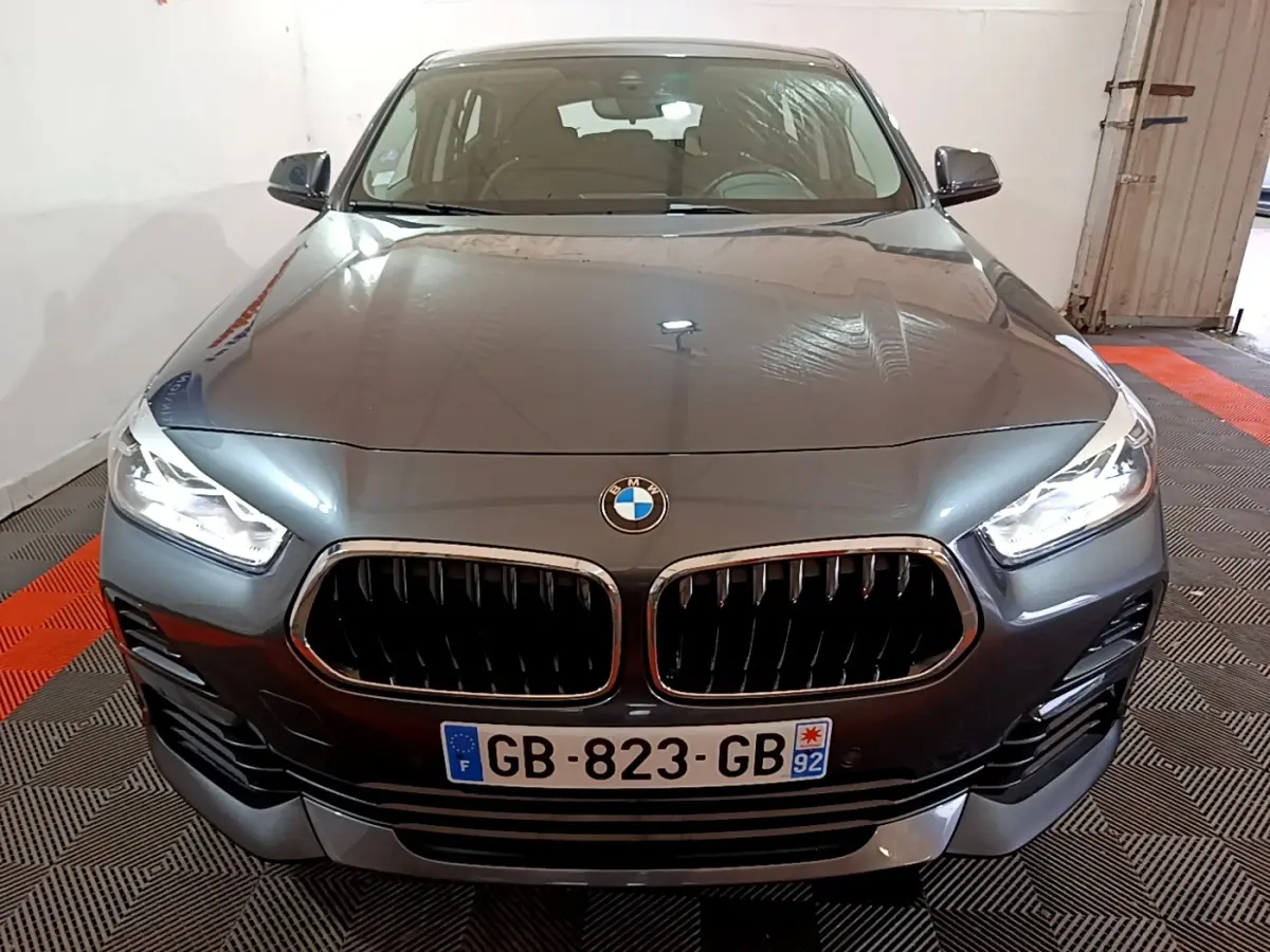 Vue frontale d'une BMW X2 sDrive18i Lounge DKG7 gris foncé avec calandre double haricot et phares LED allumés.