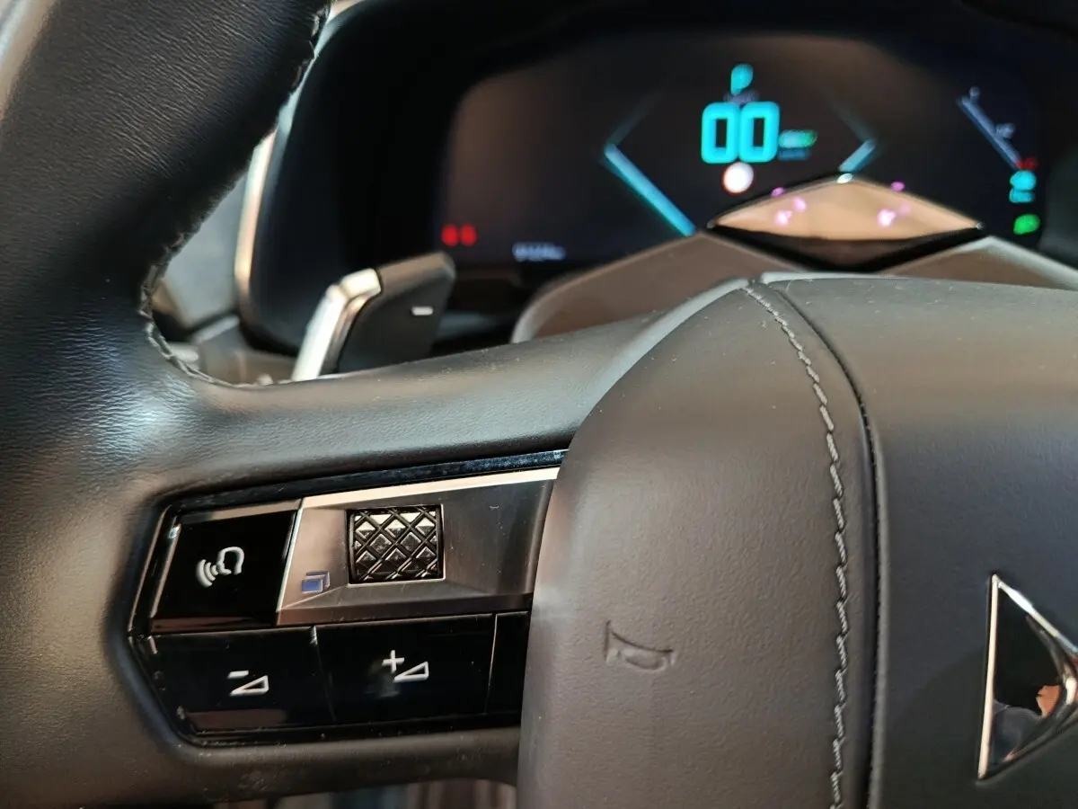 Gros plan sur la partie gauche du volant cuir noir du DS7 Crossback E-TENSE avec commandes vocales et tableau de bord numérique.