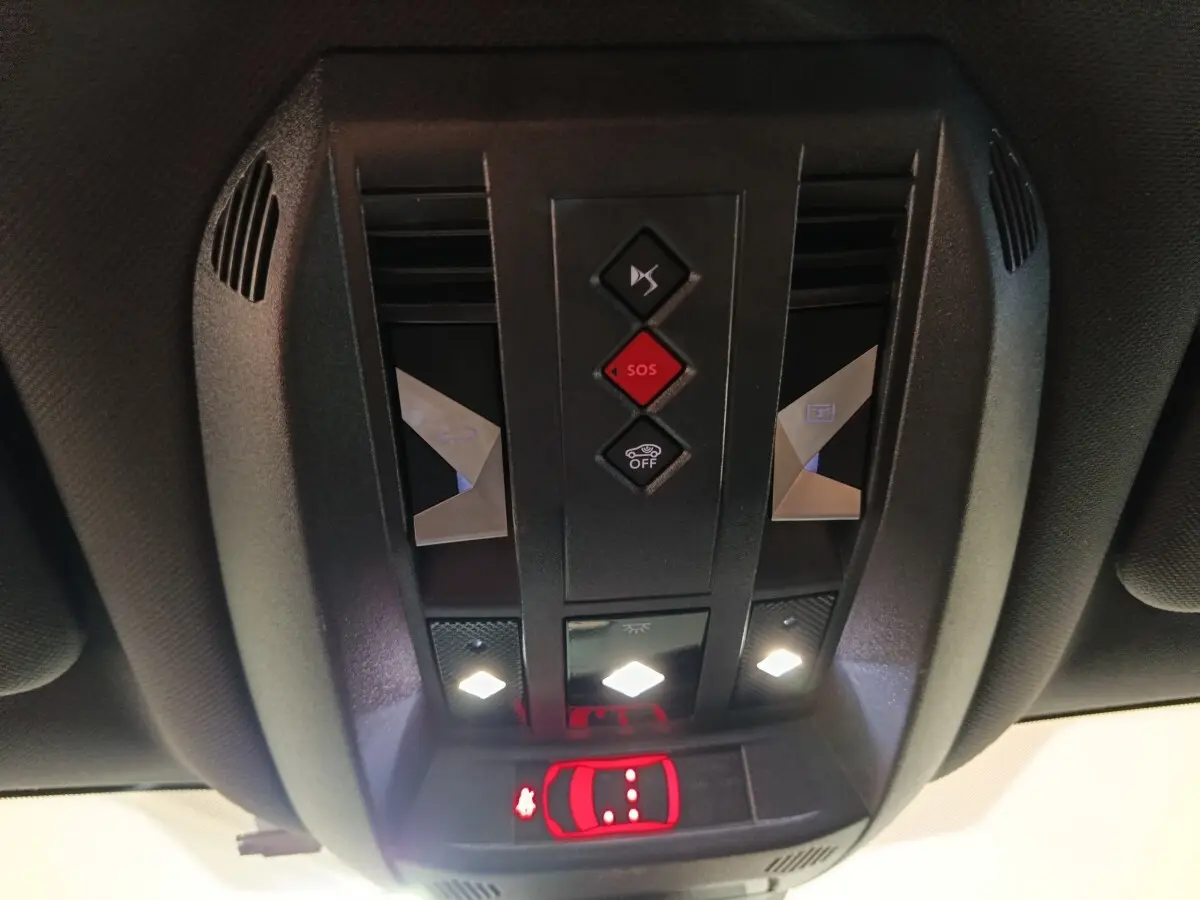 Vue en contre-plongée du panneau de commandes au plafond intérieur du DS7 Crossback noir, avec boutons SOS et éclairage LED allumé.