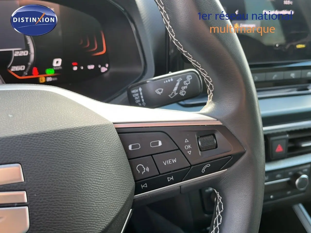 Gros plan sur le volant cuir noir avec surpiqûres blanches du SEAT Arona 2025, montrant les commandes multifonctions.
