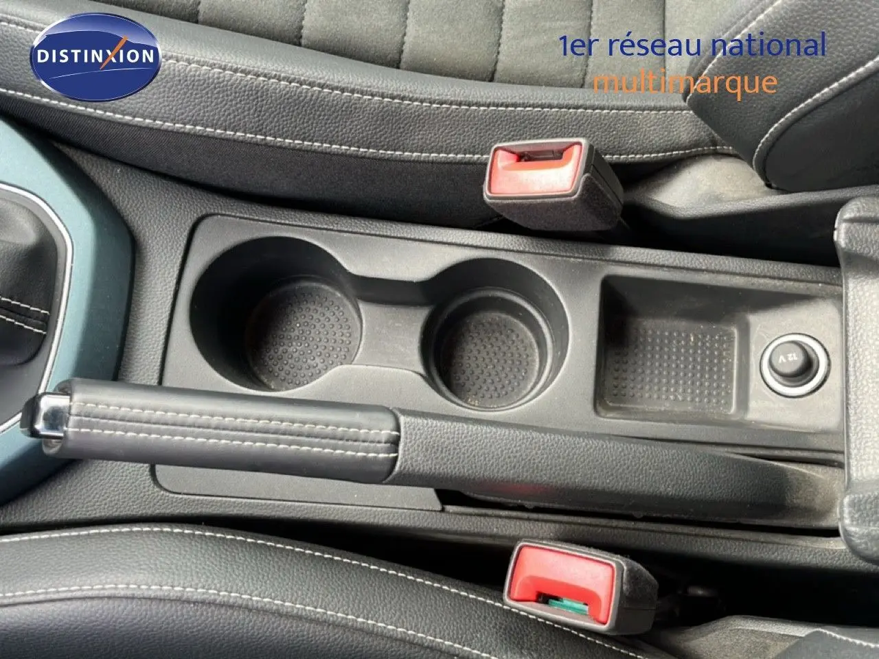 Vue rapprochée de la console centrale du SEAT Arona 2025, montrant le frein à main, porte-gobelets et bouton 12V en noir.