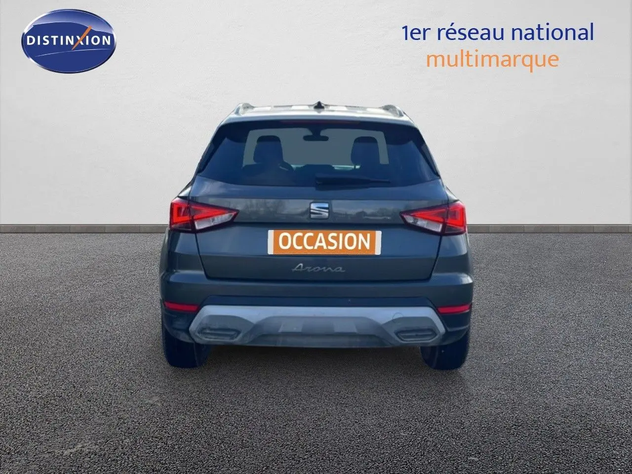 Vue arrière d'un SEAT Arona gris métallique avec toit noir, immatriculé "OCCASION" sur un sol goudronné.