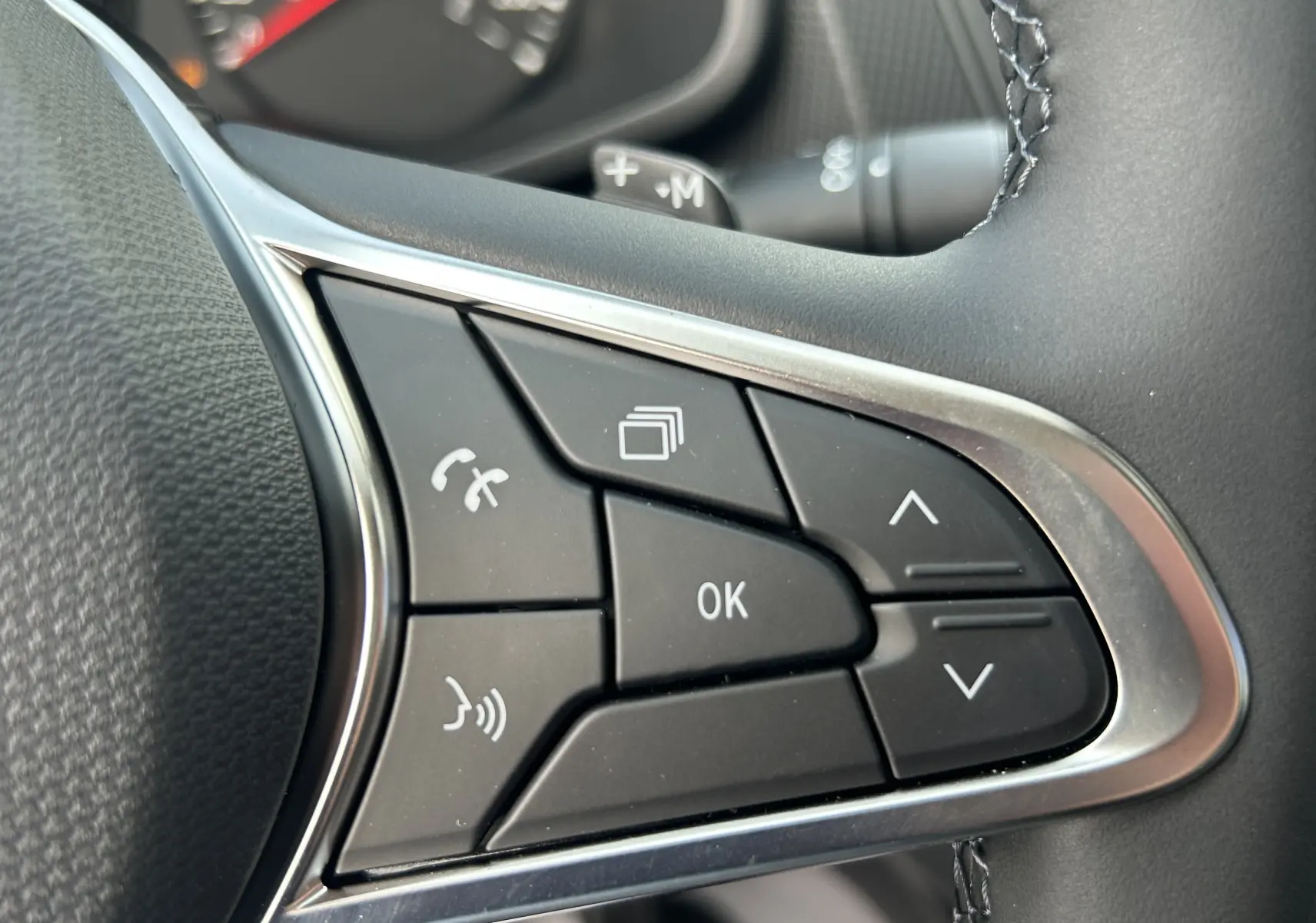 Gros plan sur les commandes multifonctions au volant côté droit du Renault Trafic Fourgon blanc, boutons noirs avec contour chromé.