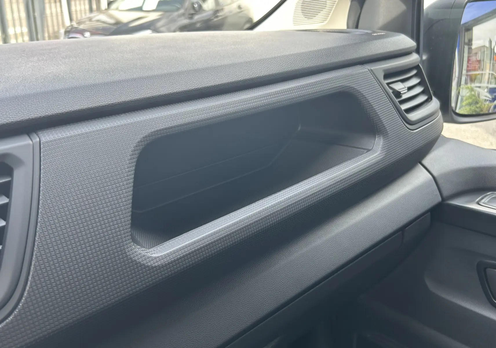 Détail intérieur du tableau de bord noir du Renault Trafic Fourgon, avec vide-poches et aérateurs visibles côté passager.