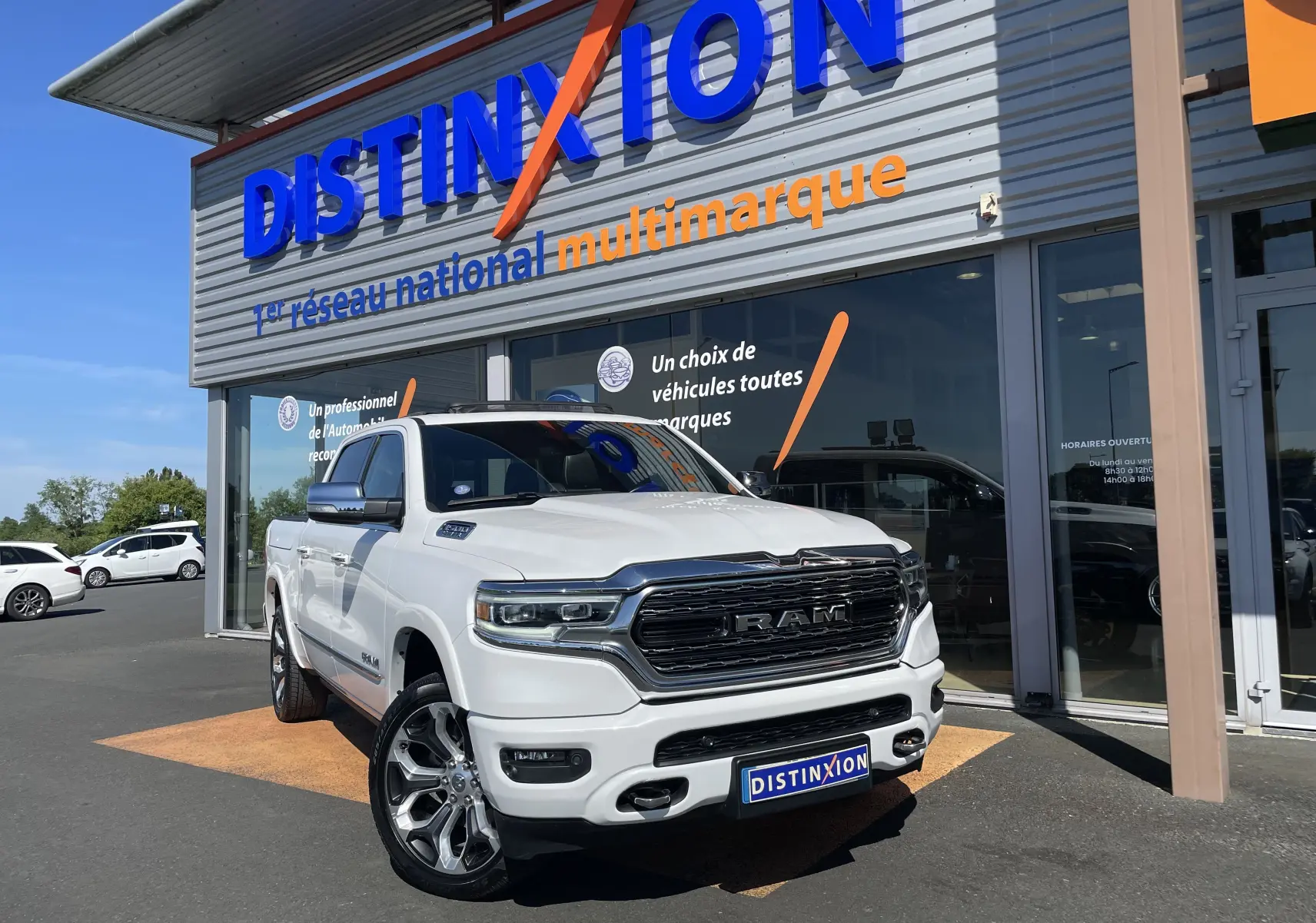 Vue 3/4 avant d’un Dodge RAM 1500 blanc nacré, avec calandre imposante et jantes alliage devant un showroom Distinxion.