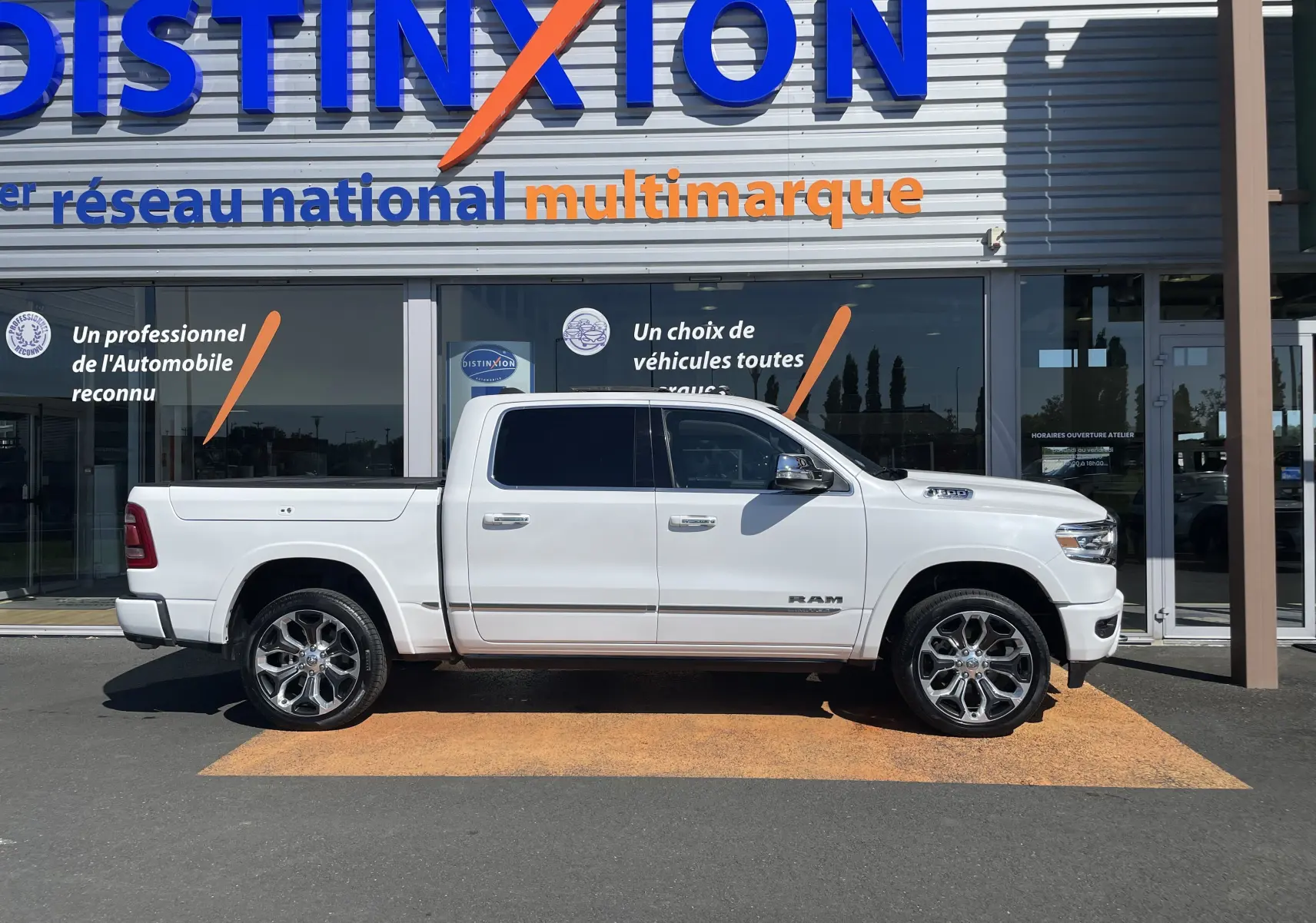 Vue de profil côté gauche d'un Dodge RAM 1500 blanc nacré avec jantes alliage et cabine double devant un showroom.