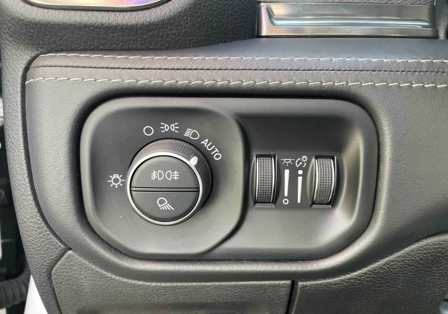 Gros plan sur les commandes d'éclairage et réglages lumineux du tableau de bord du Dodge RAM 1500 blanc nacré.