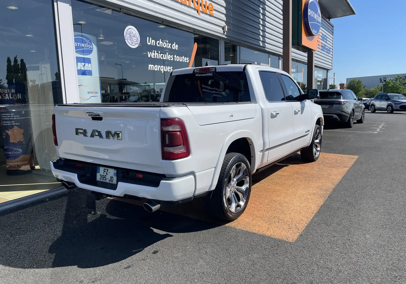 Vue 3/4 arrière droite du Dodge RAM 1500 blanc nacré avec jantes chromées et marchepied électrique visible.