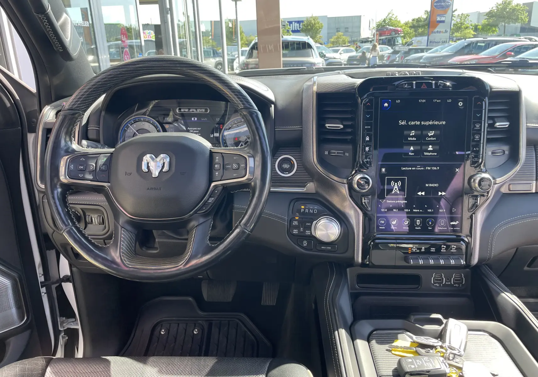 Vue intérieure du tableau de bord et volant du Dodge RAM 1500 blanc nacré avec écran tactile central et commandes au volant.