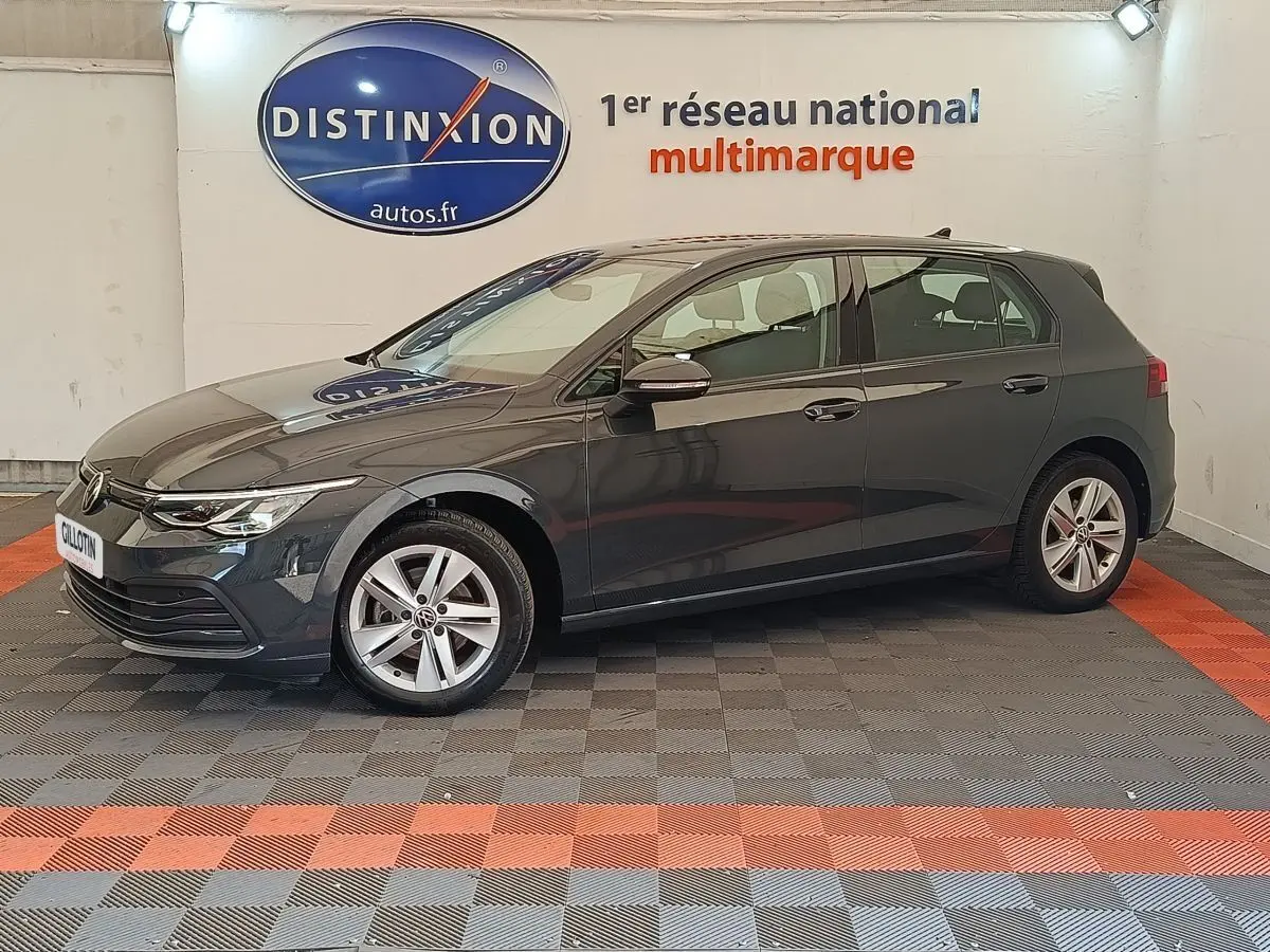 Profil droit d'une Volkswagen Golf gris foncé 2022 garée en intérieur sur sol à damier gris et rouge.