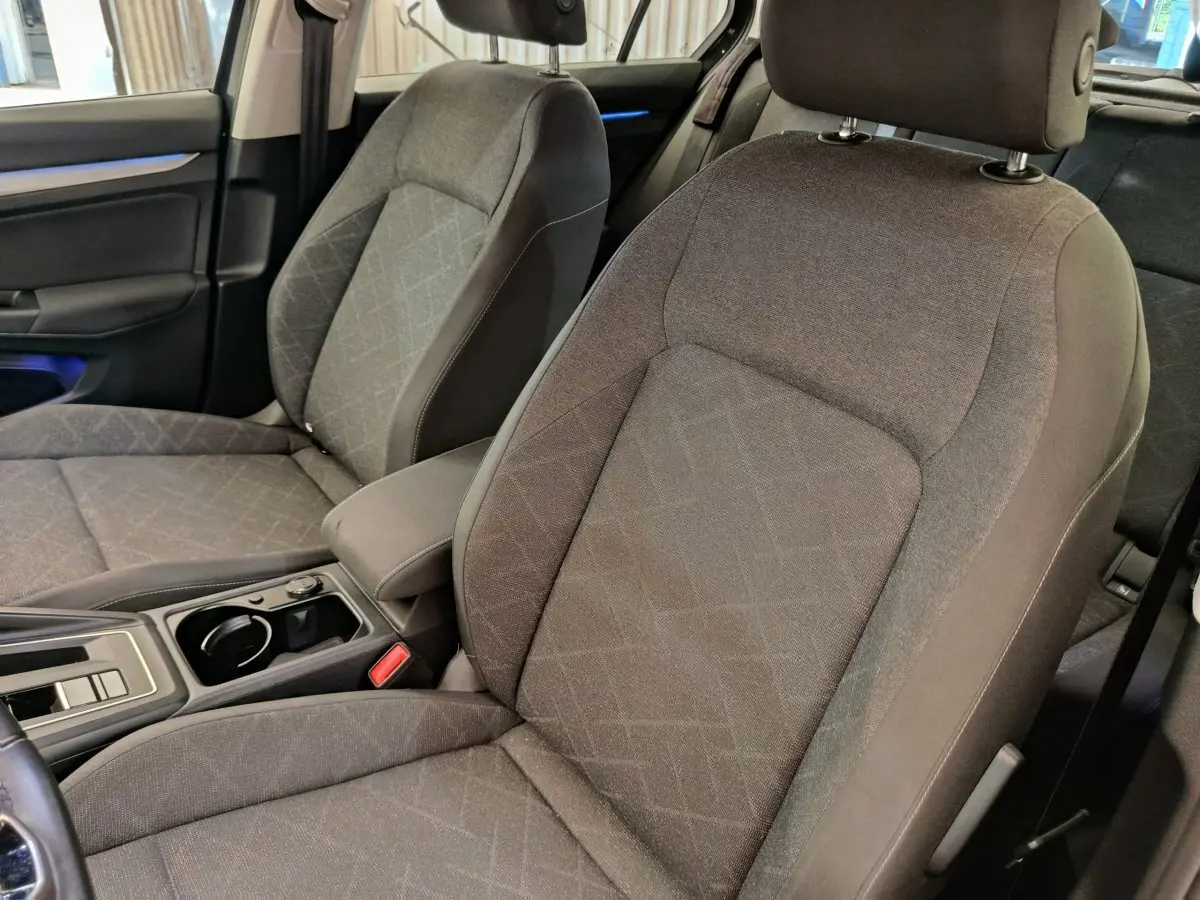 Gros plan sur les sièges avant gris tissu de la Volkswagen Golf 2022, avec accoudoir central et console moderne.