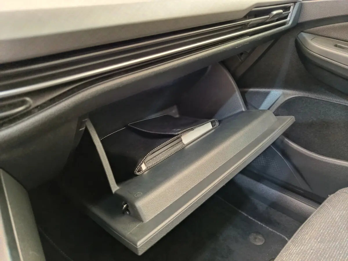 Gant de boîte à gants ouvert côté passager dans une Volkswagen Golf gris foncé, avec pochette noire visible.