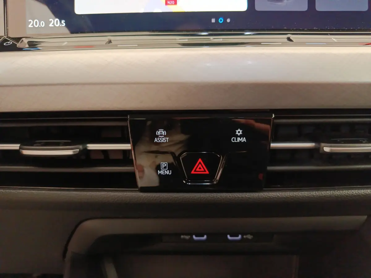 Gros plan sur la console centrale noire de la Volkswagen Golf gris foncé 2022, avec boutons d'assistance, climatisation et alerte.