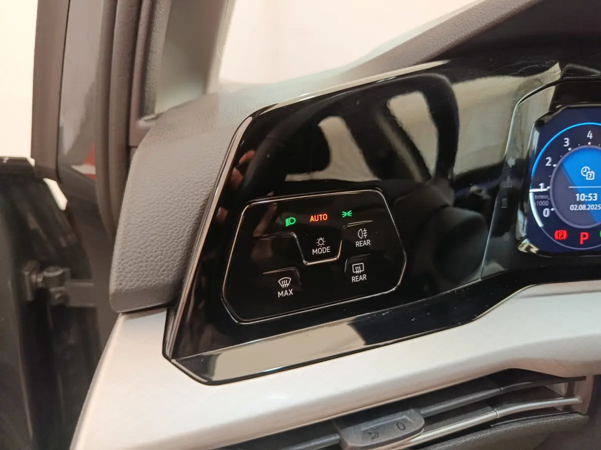 Détail du tableau de bord noir brillant côté gauche avec commandes d'éclairage et affichage digital bleu sur Volkswagen Golf gris foncé.