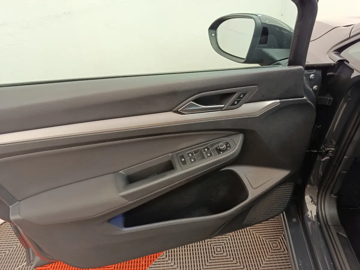 Porte côté conducteur ouverte d'une Volkswagen Golf gris foncé, montrant les commandes électriques et la poignée intérieure.