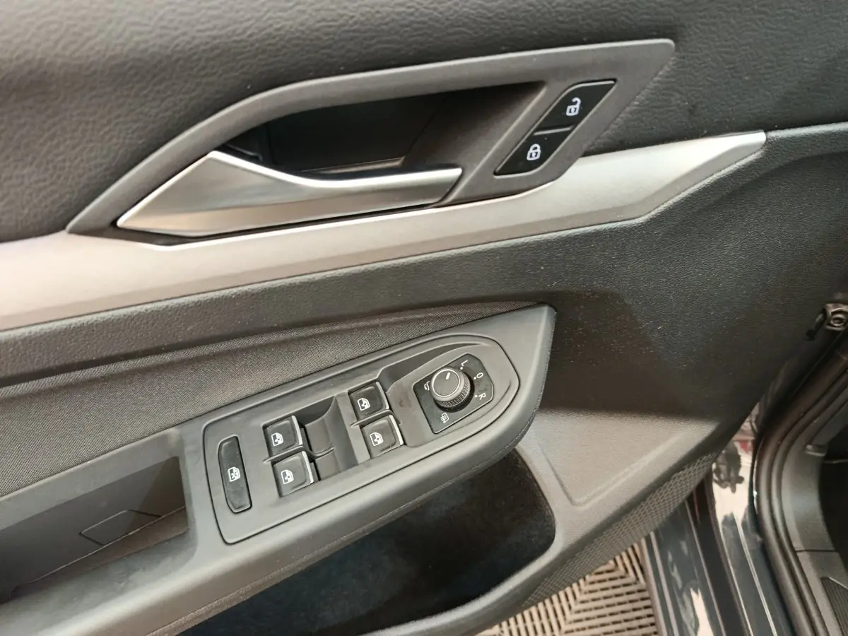 Vue rapprochée de la porte avant gauche grise d'une Volkswagen Golf 2022, avec commandes électriques et poignée argentée.
