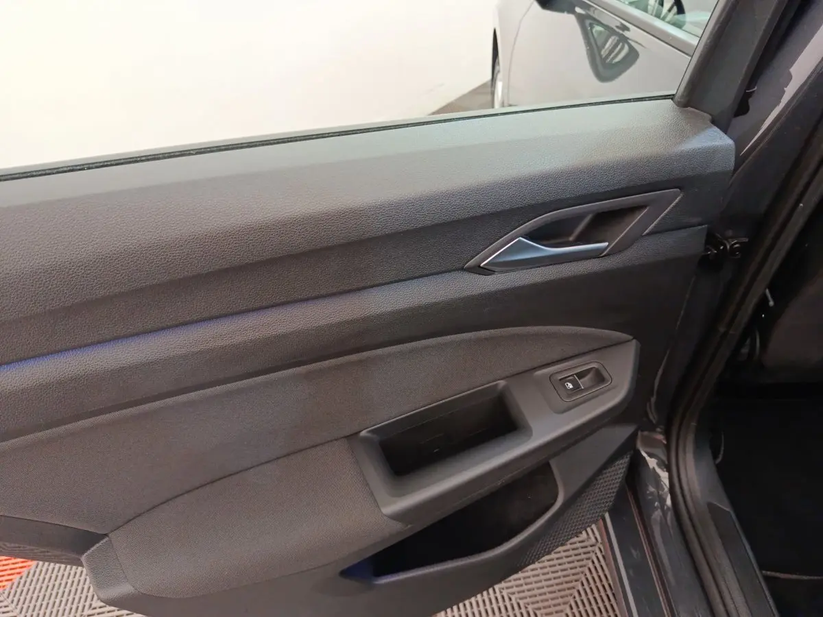 Gros plan sur la porte intérieure côté gauche de la Volkswagen Golf gris foncé, avec poignée et commande de vitre électrique.