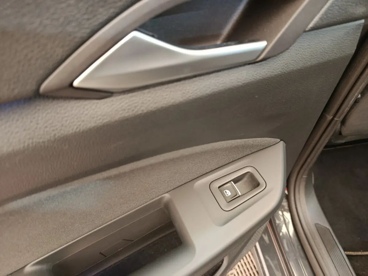 Gros plan sur la commande de lève-vitre côté conducteur de la porte intérieure d'une Volkswagen Golf gris foncé.