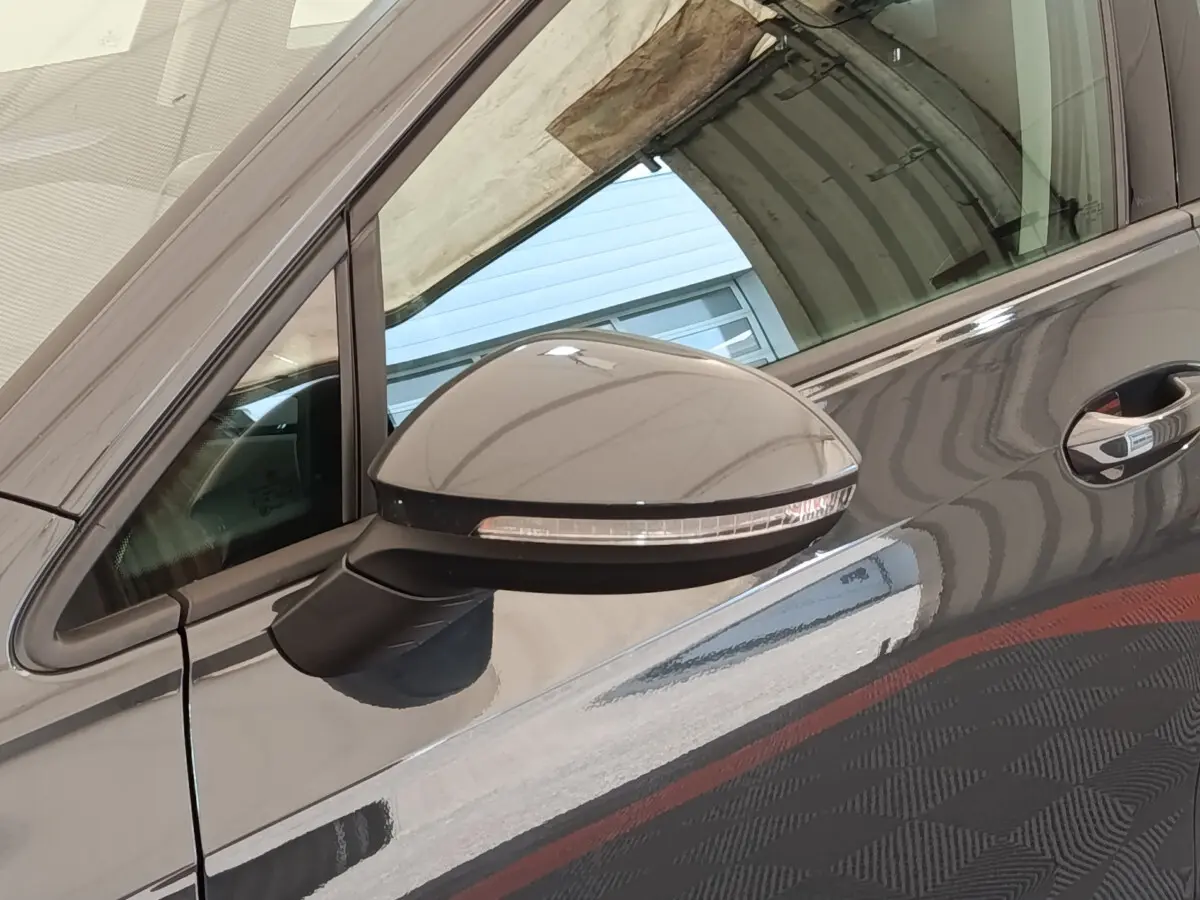 Gros plan sur le rétroviseur côté conducteur d’une Volkswagen Golf gris foncé reflétant l’environnement autour.