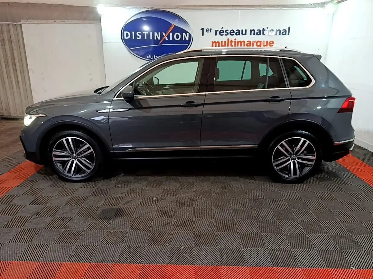 Vue latérale droite d'un Volkswagen Tiguan gris clair 2022 dans un showroom avec jantes alliage et feux allumés.